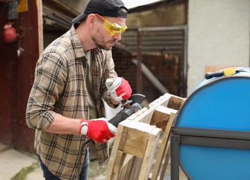 Photo of Man grinding wooden planks with angle grinder outdoors