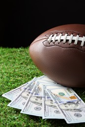 Photo of American football ball and dollar banknotes on green grass