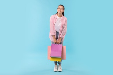 Photo of Smiling woman with colorful shopping bags on light blue background