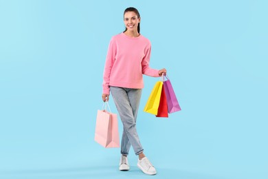 Photo of Smiling woman with colorful shopping bags on light blue background