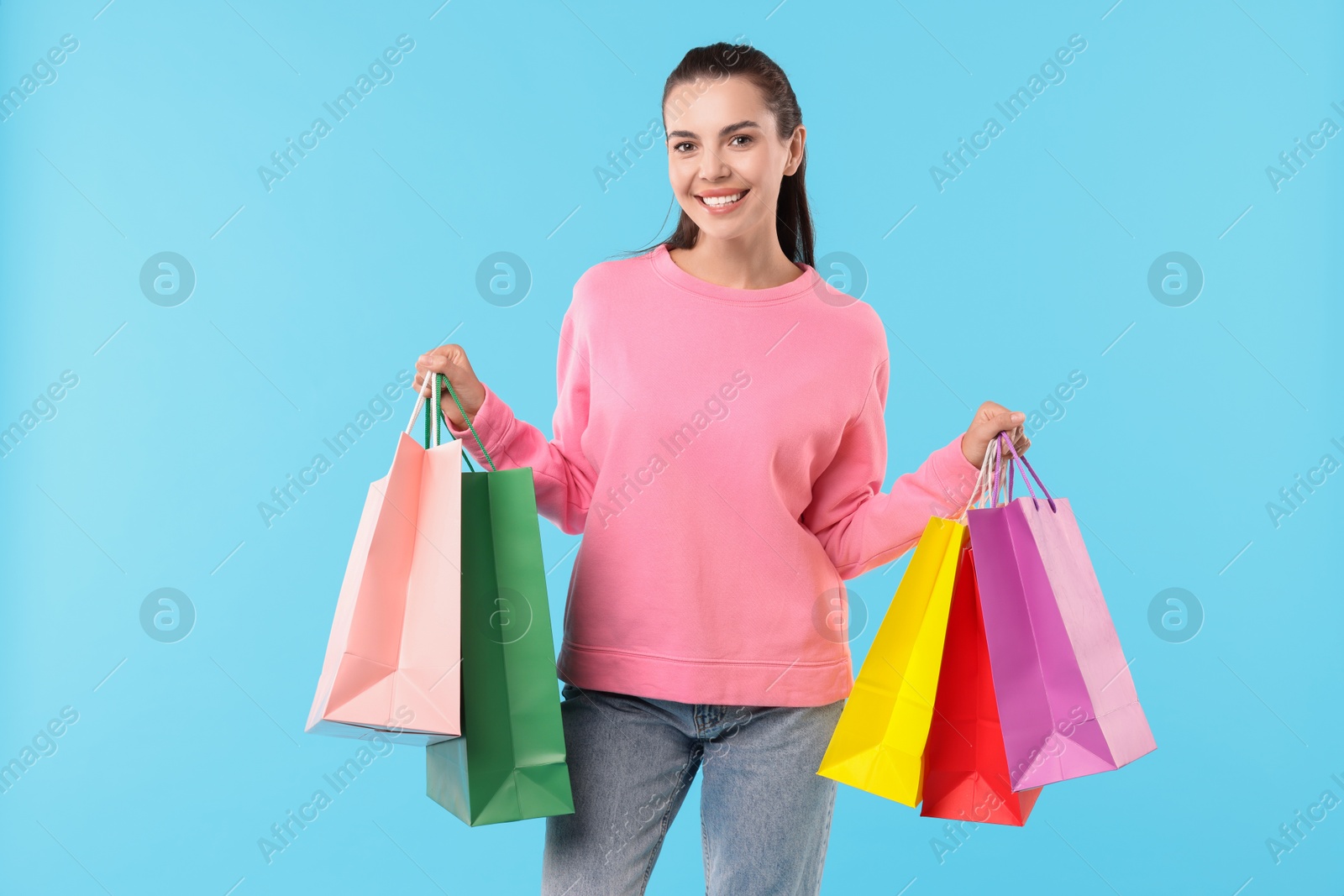 Photo of Smiling woman with colorful shopping bags on light blue background