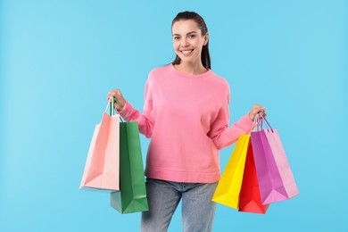 Photo of Smiling woman with colorful shopping bags on light blue background