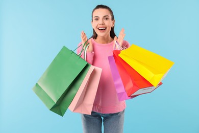 Photo of Happy woman with colorful shopping bags on light blue background