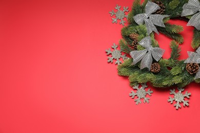 Photo of Christmas wreath with snowflakes, cones and bows on red background, flat lay. Space for text