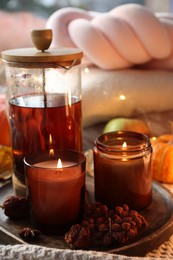 Photo of Burning candles, freshly brewed tea and autumn decor on fabric