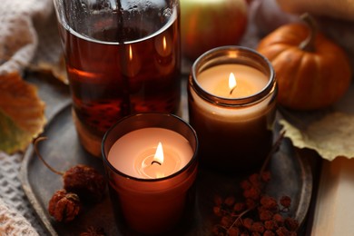 Photo of Burning candles, freshly brewed tea and autumn decor on fabric, closeup