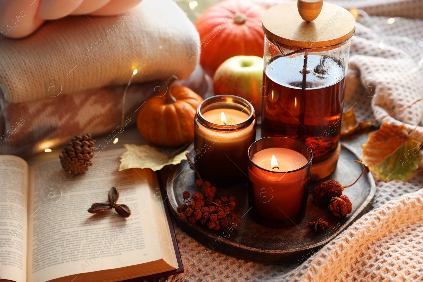 Photo of Burning candles, freshly brewed tea, sweaters, book and autumn decor on fabric