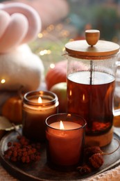 Photo of Burning candles, freshly brewed tea and autumn decor on fabric, closeup