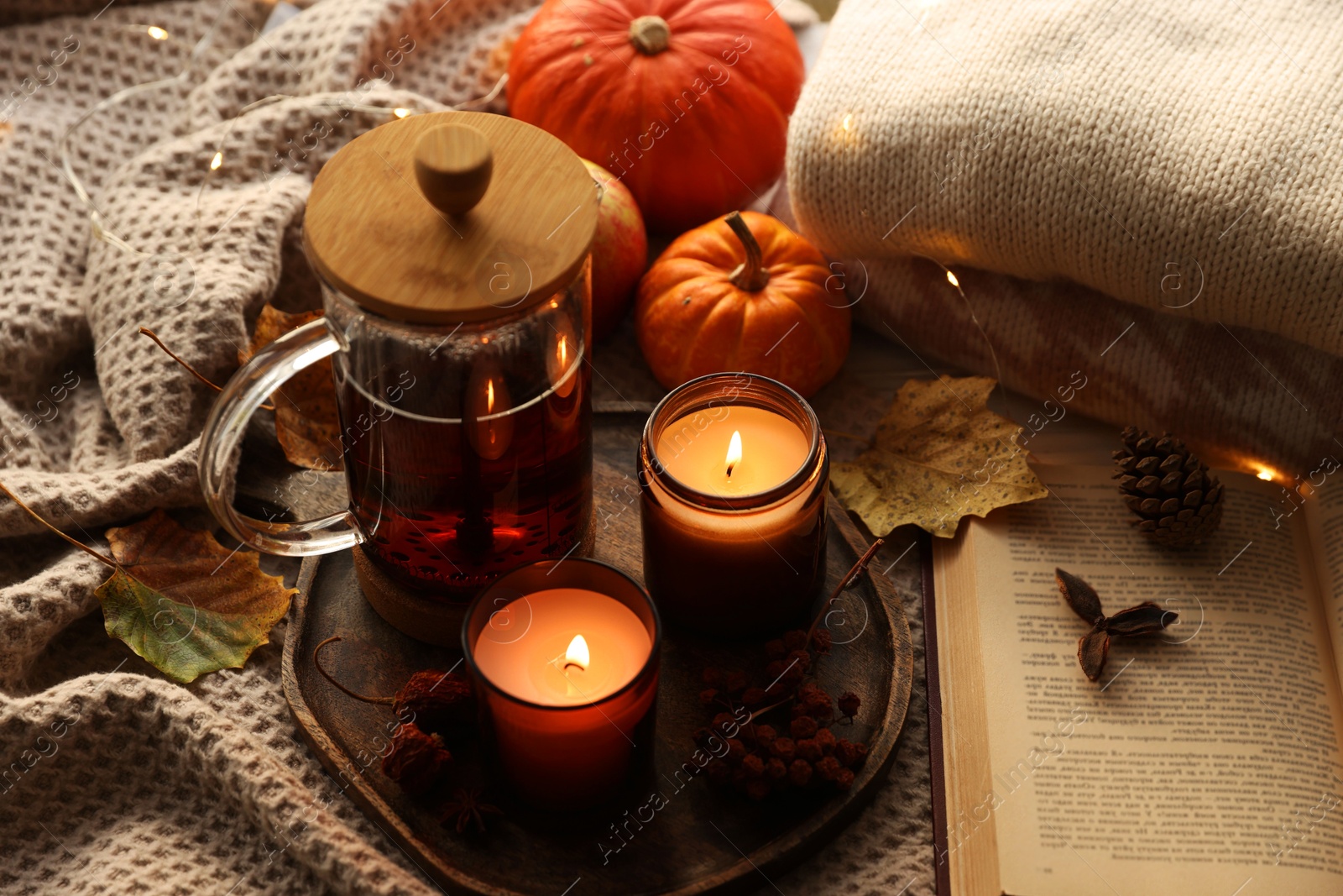 Photo of Burning candles, freshly brewed tea, sweaters, book and autumn decor on fabric