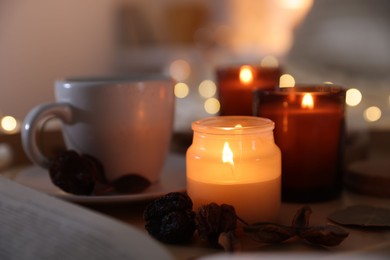 Photo of Burning candles, cup of drink and decor on tray indoors, closeup. Autumn atmosphere