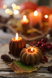 Photo of Burning candles in shape of pumpkins, old book and autumn decor on table, closeup