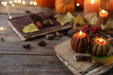 Photo of Burning candles in shape of pumpkins, old book and autumn decor on wooden table, closeup