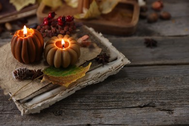 Photo of Burning candles in shape of pumpkins, old book and autumn decor on wooden table, closeup