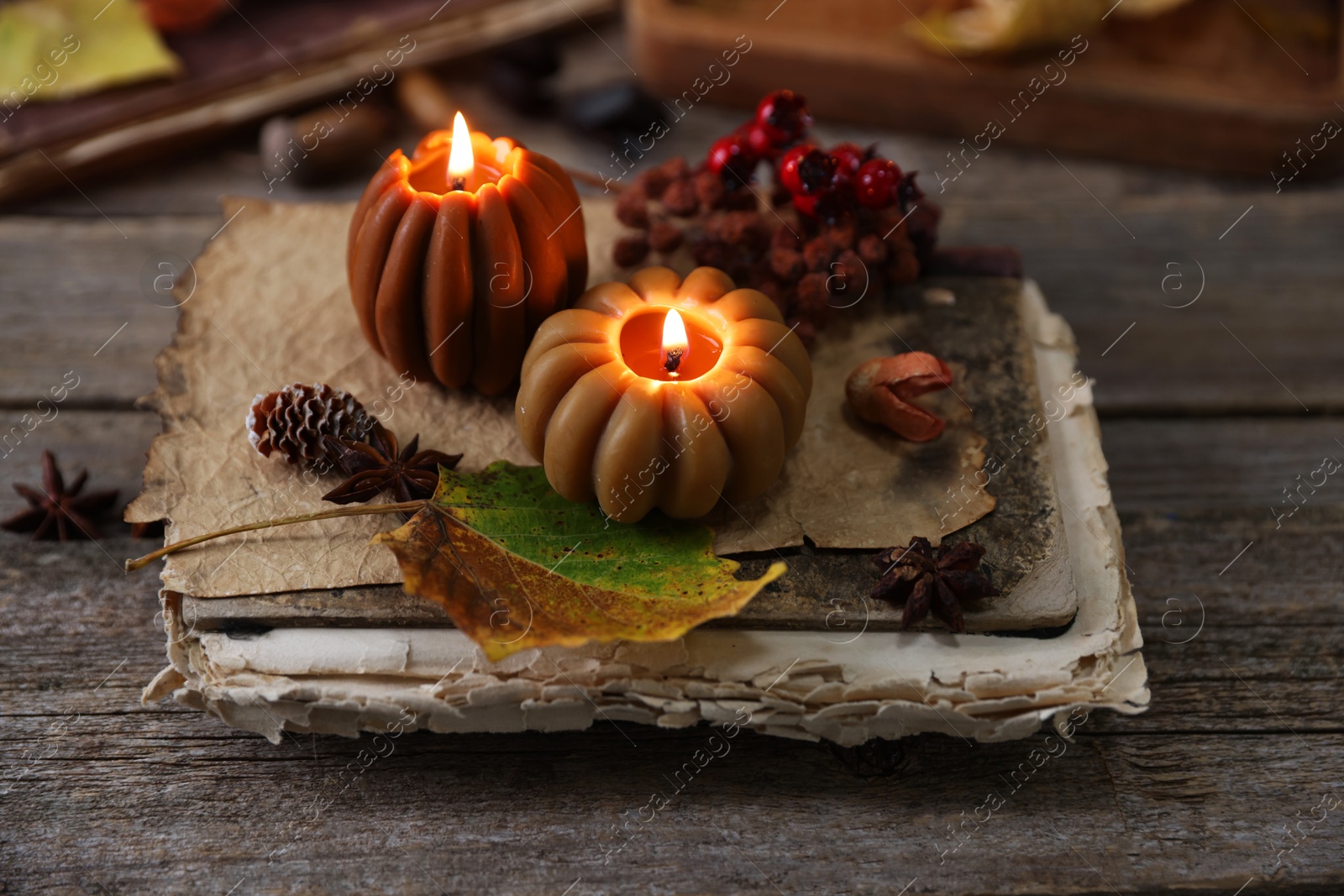 Photo of Burning candles in shape of pumpkins, old book and autumn decor on wooden table