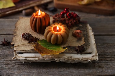 Photo of Burning candles in shape of pumpkins, old book and autumn decor on wooden table