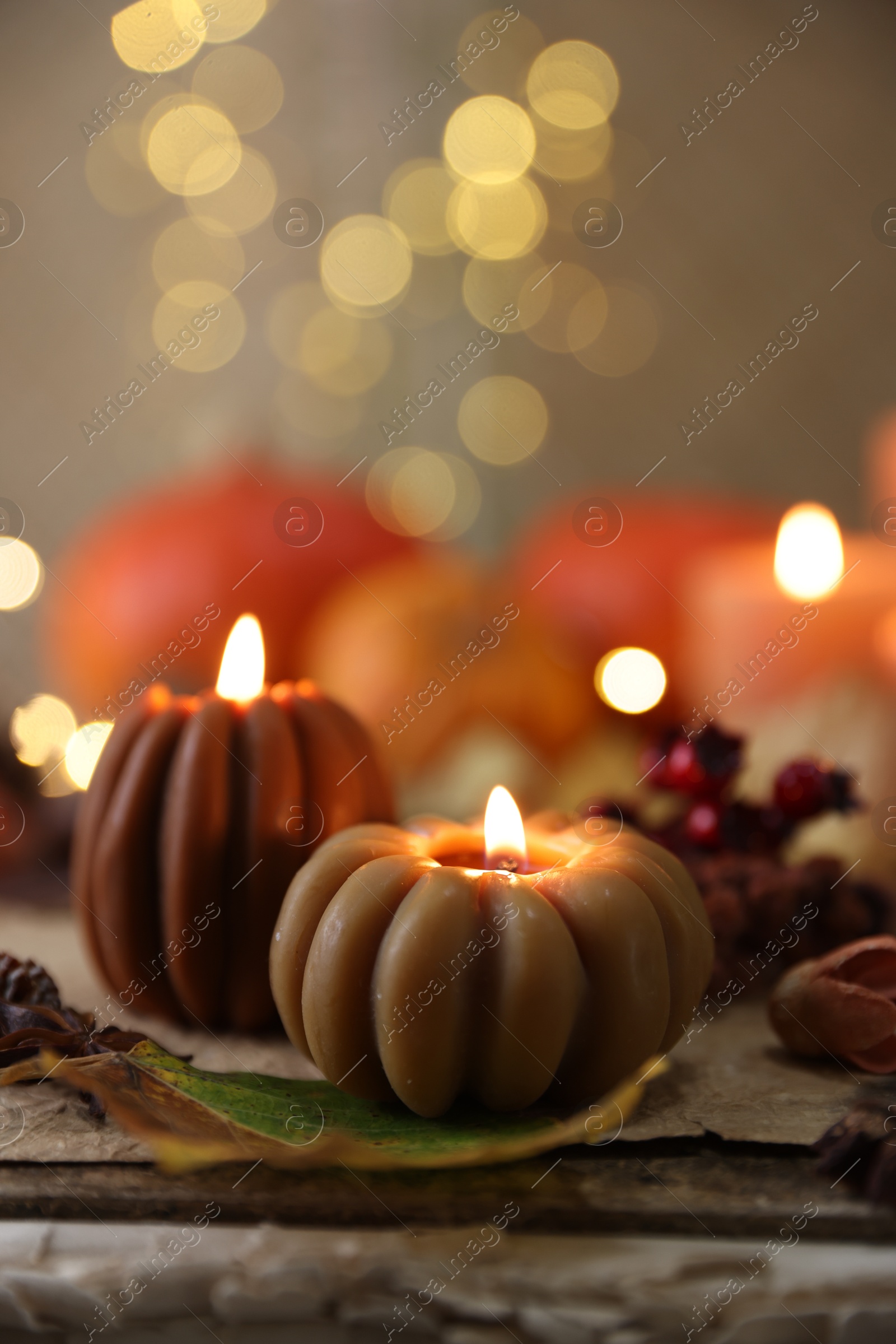 Photo of Burning candles in shape of pumpkins and autumn decor on table, closeup