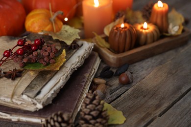 Photo of Autumn decor, old books and burning candles in shape of pumpkins on wooden table, closeup