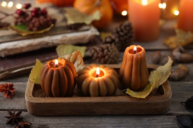 Photo of Burning candles in shape of pumpkins and autumn decor on wooden table