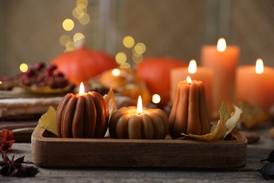 Photo of Burning candles in shape of pumpkins and autumn decor on wooden table