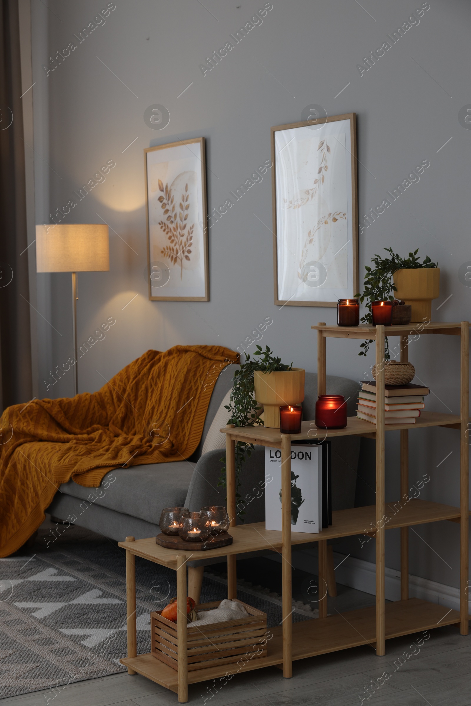 Photo of Burning candles, houseplants and stylish furniture in cozy room