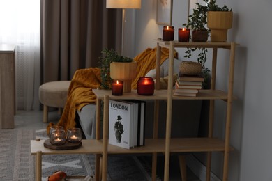 Photo of Shelving unit with burning candles, houseplants and books in cozy room