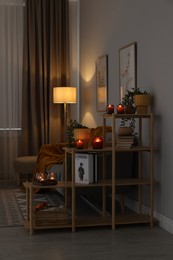 Photo of Shelving unit with burning candles, houseplants and books in cozy room