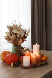 Photo of Tray with many burning candles and autumn decor on wooden table indoors