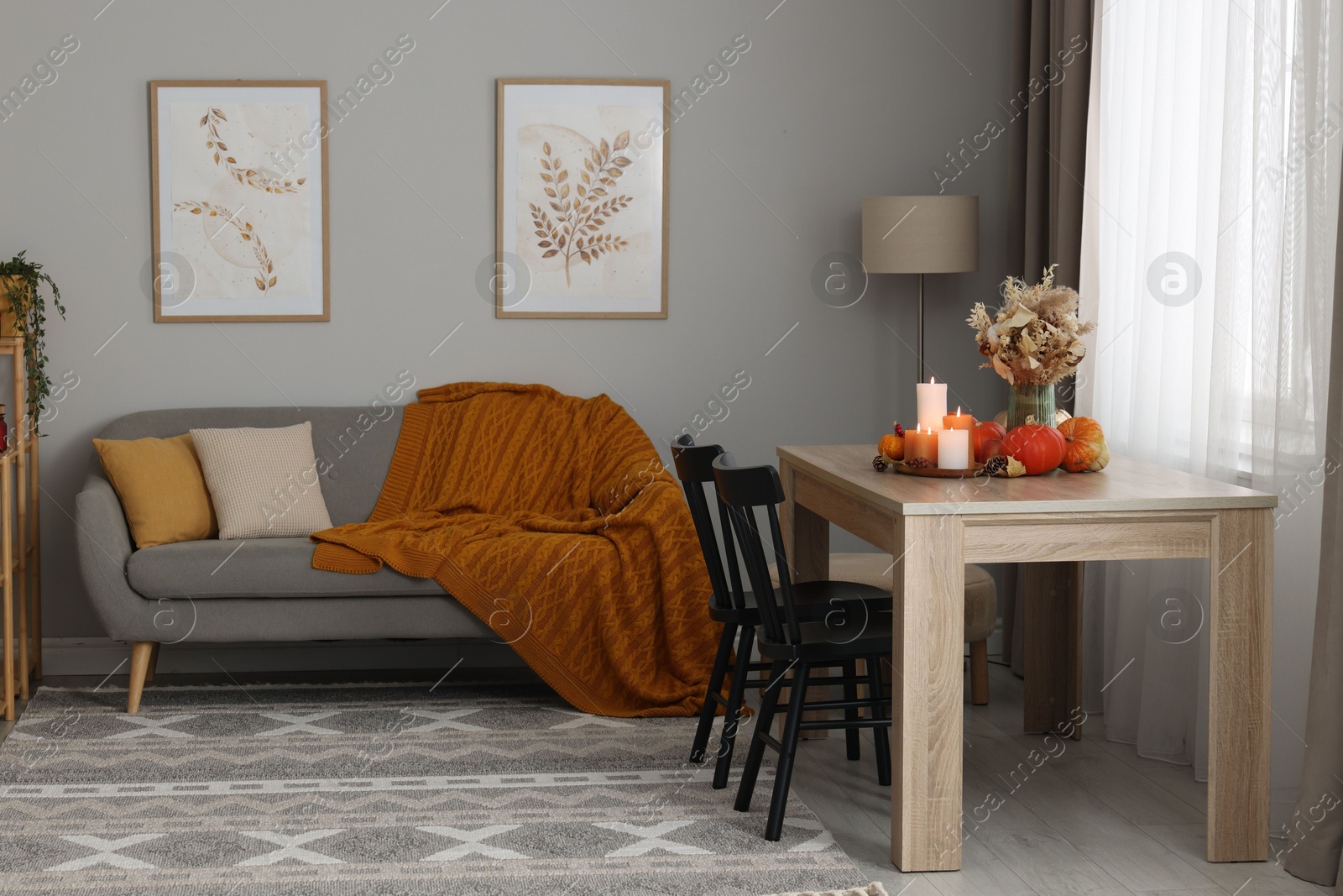 Photo of Burning candles and stylish furniture in cozy room. Autumn atmosphere