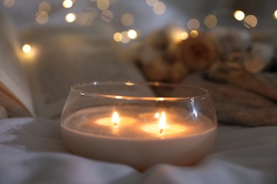 Photo of Burning candle on white cloth, closeup. Cozy atmosphere