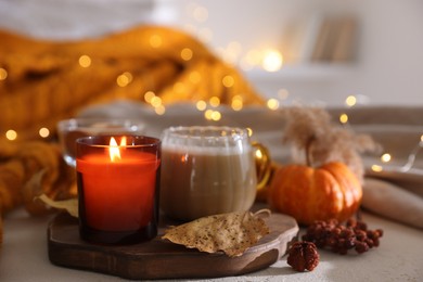 Photo of Burning candle and autumn decor on light table, closeup. Cozy atmosphere