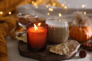 Photo of Burning candle and autumn decor on light table, closeup. Cozy atmosphere