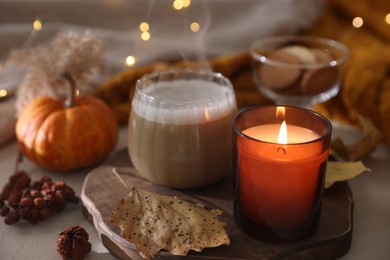 Photo of Burning candle, cocoa and autumn decor on light table, closeup. Cozy atmosphere