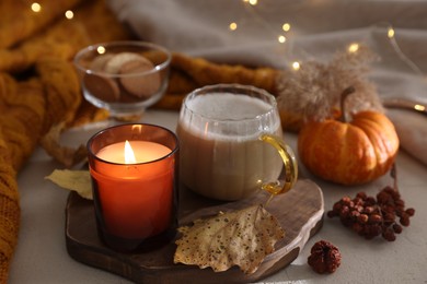 Burning candle, cocoa and autumn decor on light table. Cozy atmosphere