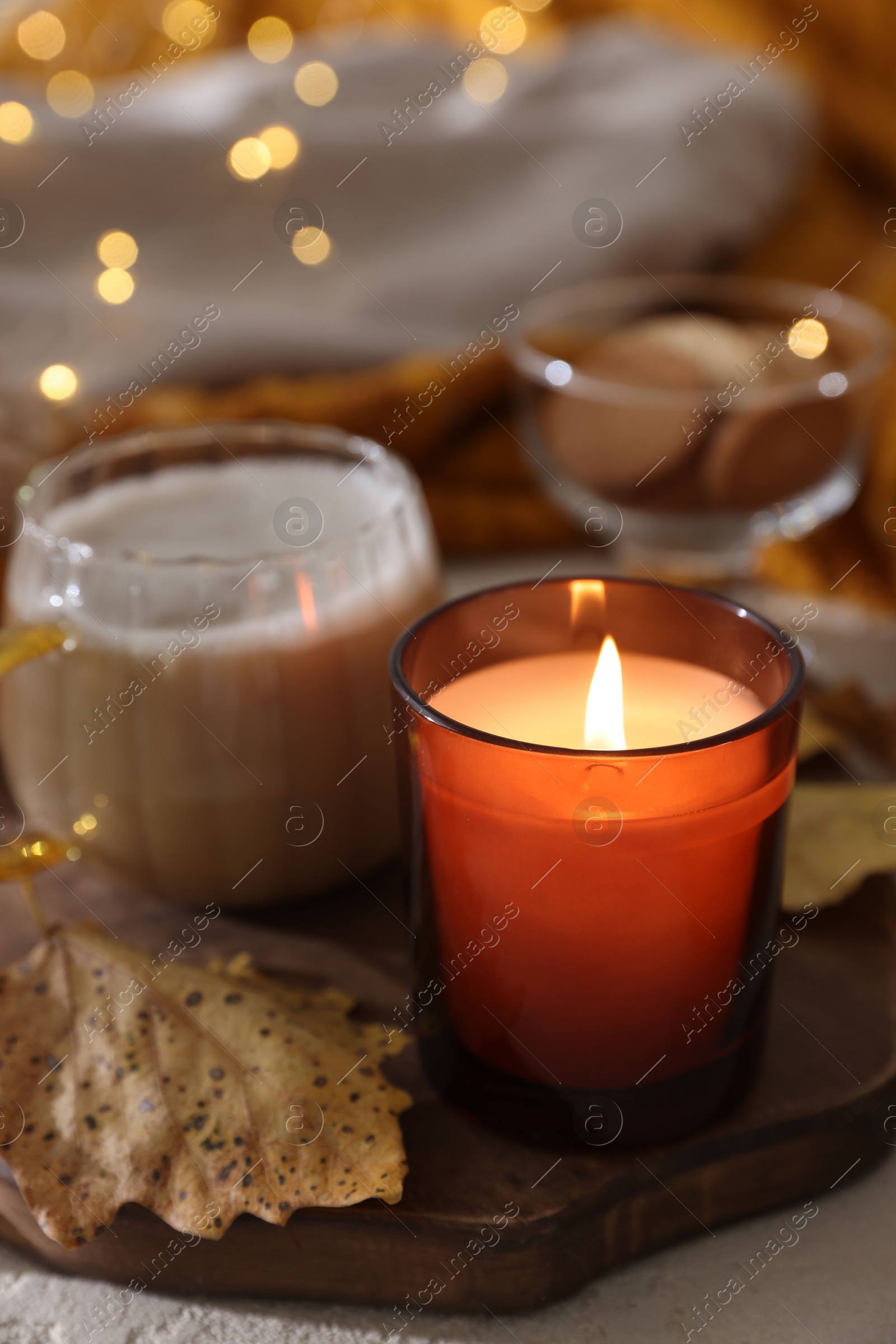 Photo of Burning candle, cocoa and dry leaves on table, closeup. Autumn atmosphere