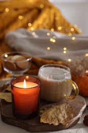 Photo of Burning candle, cocoa and dry leaves on table, closeup. Autumn atmosphere