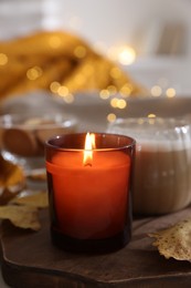 Photo of Burning candle, cocoa and dry leaves on table, closeup. Autumn atmosphere