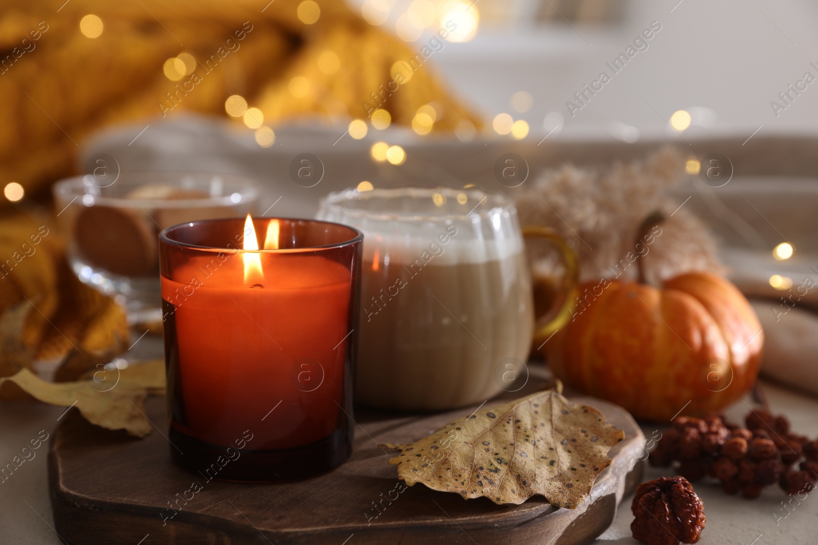 Photo of Burning candle, cocoa and dry leaves on table, closeup. Autumn atmosphere