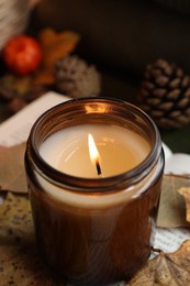 Burning candle and dry leaves on blurred background, closeup. Autumn atmosphere