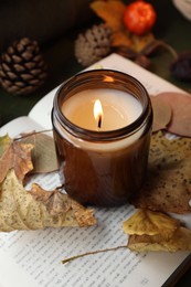 Photo of Burning candle and dry leaves on open book, closeup. Autumn atmosphere