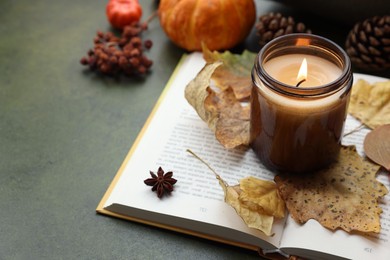 Photo of Burning candle, autumn decor and open book on green background. Space for text