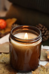 Photo of Burning candle and dry leaves on open book, closeup. Autumn atmosphere