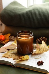 Photo of Burning candle, autumn decor and open book on green background