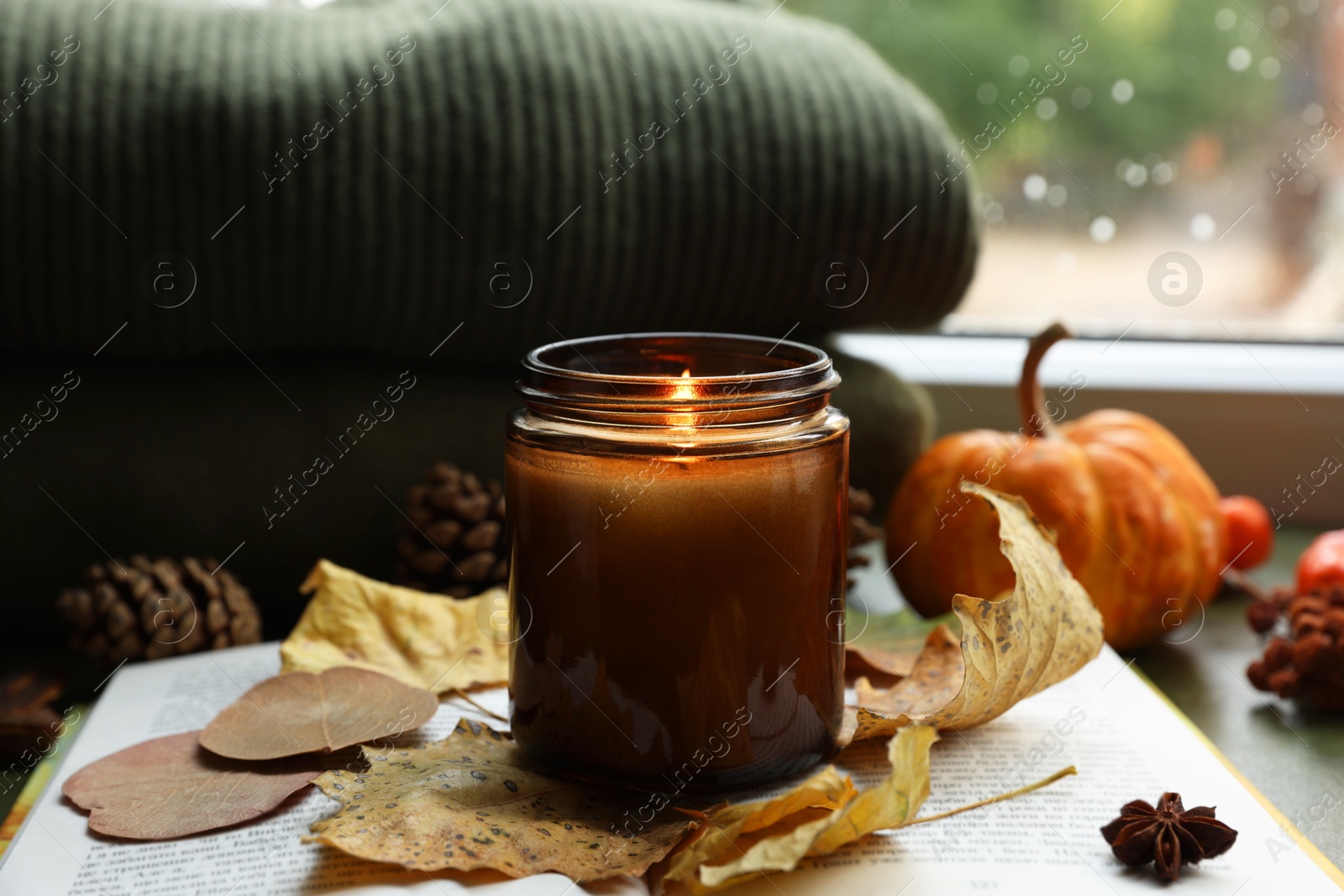 Photo of Burning candle and dry leaves on open book, closeup. Autumn atmosphere