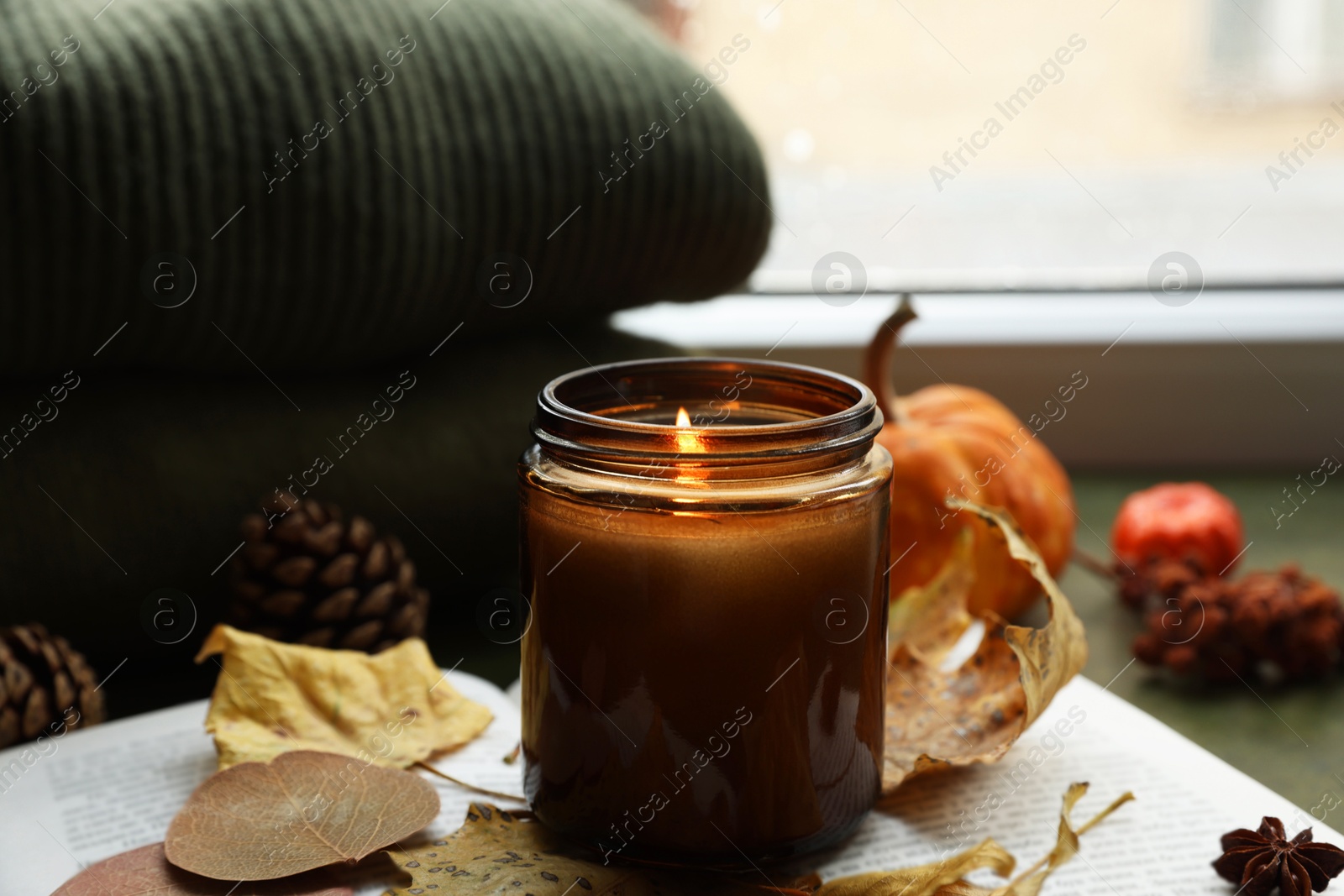 Photo of Burning candle and dry leaves on open book, closeup. Autumn atmosphere