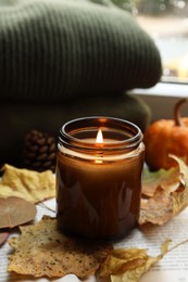 Photo of Burning candle and dry leaves on open book. Autumn atmosphere