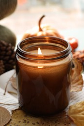 Photo of Burning candle and dry leaves on open book, closeup. Autumn atmosphere