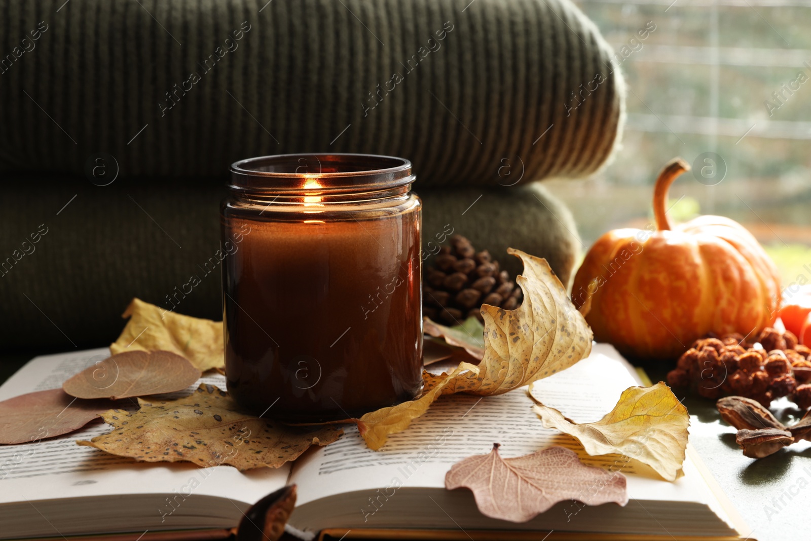 Photo of Burning candle and dry leaves on open book, closeup. Autumn atmosphere