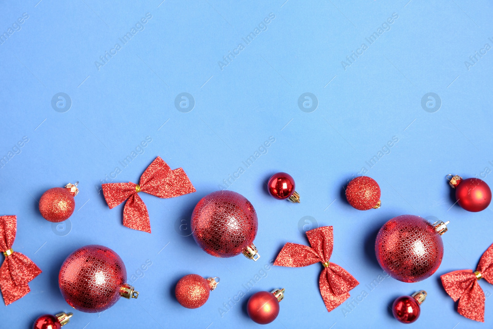 Photo of Christmas balls and bows on light blue background, flat lay. Space for text