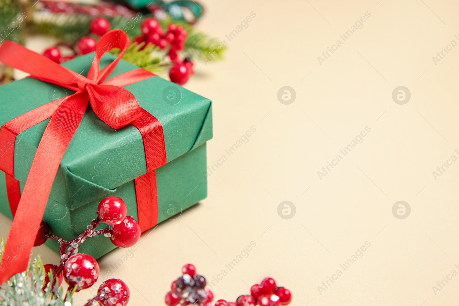 Photo of Christmas gift box, berries and fir tree branches on beige background, closeup. Space for text