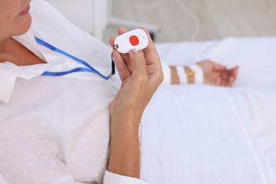 Senior woman with emergency call button on bed in hospital, closeup